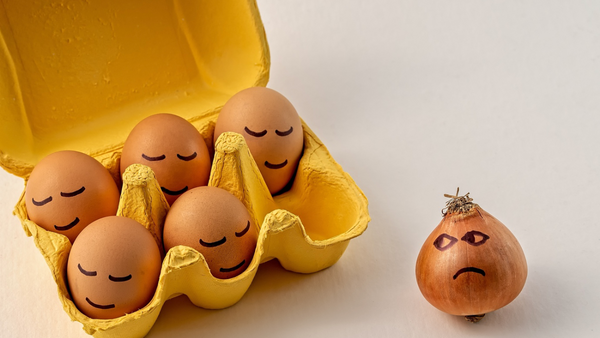 5 Eggs in a box with smiling faces. One onion outside the box looking at the eggs with a sad face.